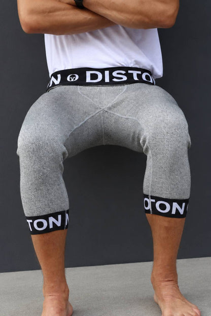 A person wearing gray heathered compression shorts with black elastic waistband and cuffs featuring white 'DISTON' branding, shown from the waist down against a dark gray background.