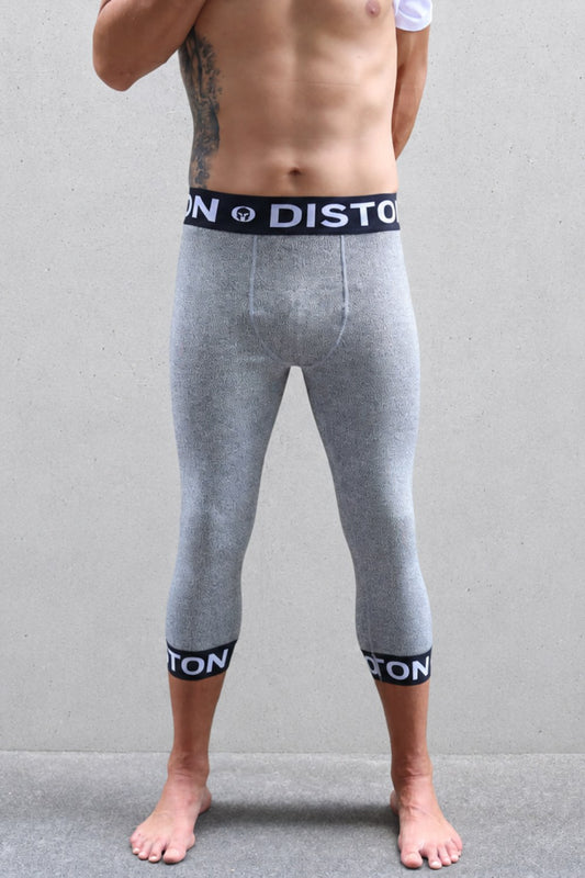 A man ski racer wearing heather gray full-length compression leggings with black elastic cuffs and a matching waistband featuring the white 'DISTON' brand logo, standing against a gray wall.